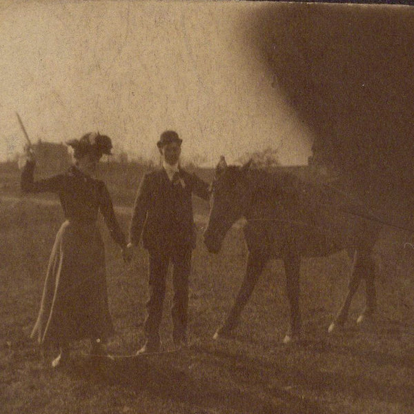 Snapshot of a woman and man holding hands, the woman raises a whip to a horse, the photographer's finger blocks the lens (cabinet card photograph)