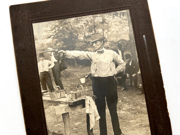 Photograph of a man in a bowtie and hat shooting at an unseen target, ca. 1910-1920