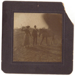 Snapshot of a woman and man holding hands, the woman raises a whip to a horse, the photographer's finger blocks the lens (cabinet card photograph)