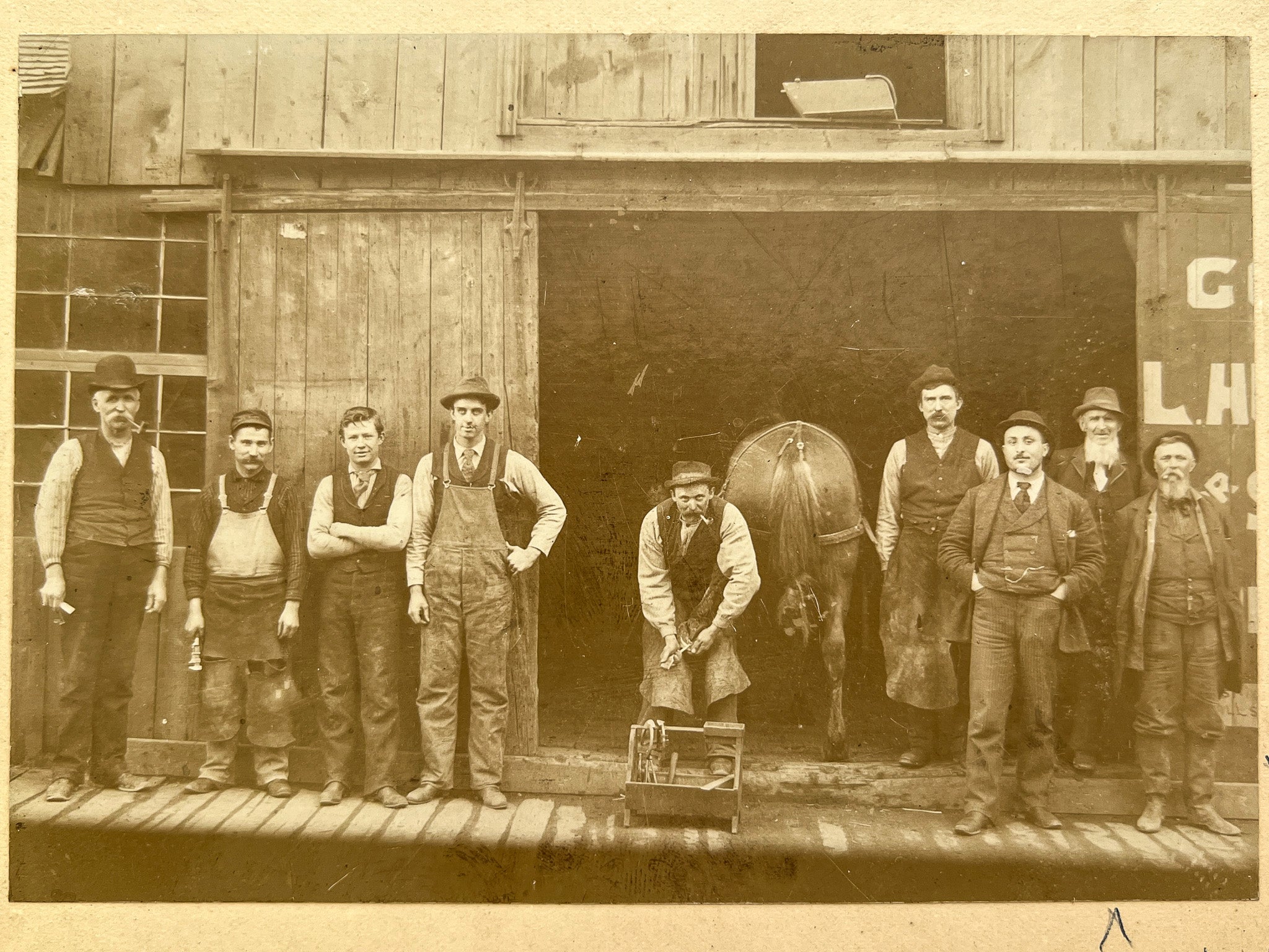 Occupational portrait of nine farriers, a horse's rear, and a child in the shadows, ca. 1900