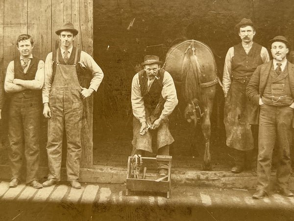 Occupational portrait of nine farriers, a horse's rear, and a child in the shadows, ca. 1900