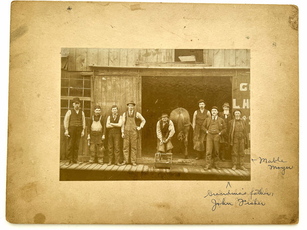 Occupational portrait of nine farriers, a horse's rear, and a child in the shadows, ca. 1900