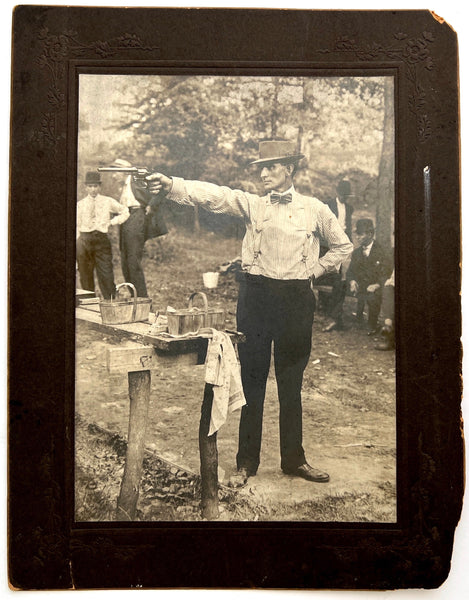 Photograph of a man in a bowtie and hat shooting at an unseen target, ca. 1910-1920