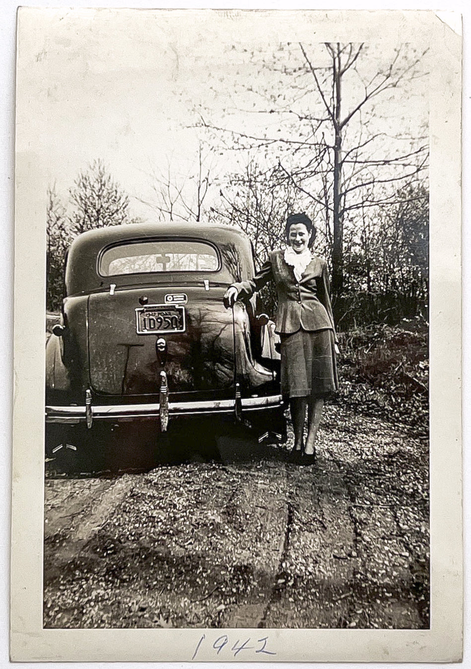 1942 snapshot of a woman posed next to a National Defense automobile